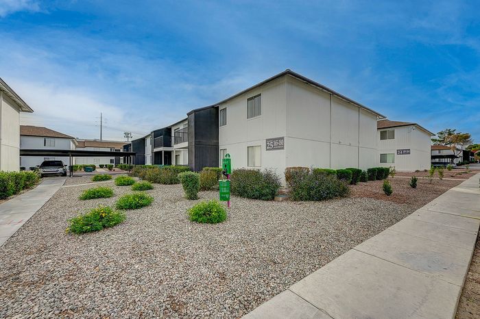 Inviting apartment complex exterior with modern architecture, well-maintained greenery, and accessible walkways under a bright blue sky.