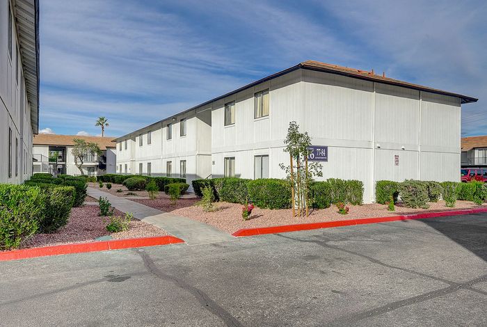 Modern apartment complex with manicured landscaping and paved walkways under a bright blue sky, offering a welcoming and serene living environment.