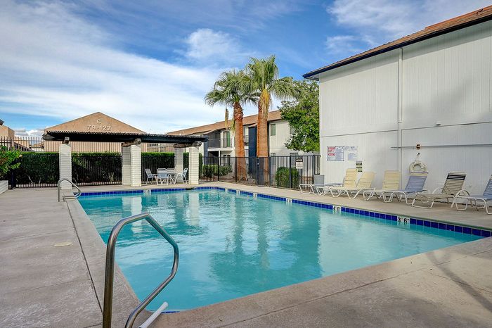 Inviting apartment complex pool area with lounge chairs, lush palm trees, and serene surroundings, perfect for relaxation and enjoyment.
