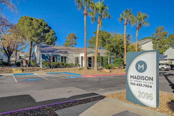 Inviting entrance of Madison at Green Valley, showcasing a serene landscape with palm trees and modern architecture under a clear blue sky.
