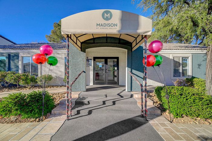 Inviting entrance of Madison at Green Valley featuring a covered awning and festive balloons, surrounded by lush greenery and bright blue skies.