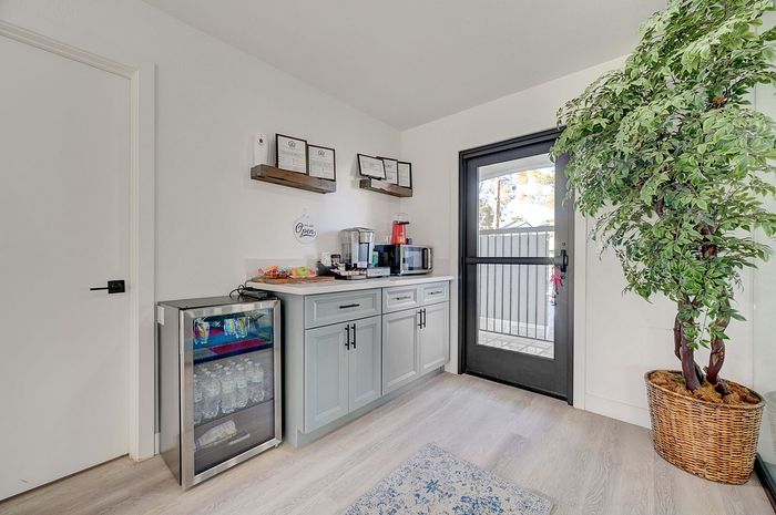 Inviting refreshment nook with elegant cabinetry, mini fridge, and large potted plant, leading to outdoor space.