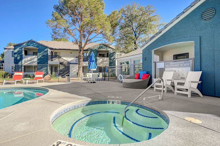 Inviting apartment complex featuring a sparkling pool area with jacuzzi, vibrant seating, and lush outdoor space under a clear blue sky.