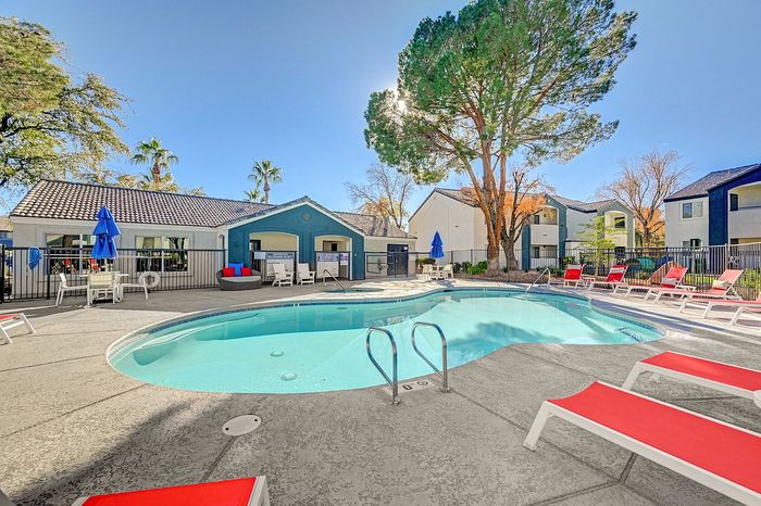 Bright outdoor pool area with modern lounge chairs and a backdrop of trees and charming residential buildings.