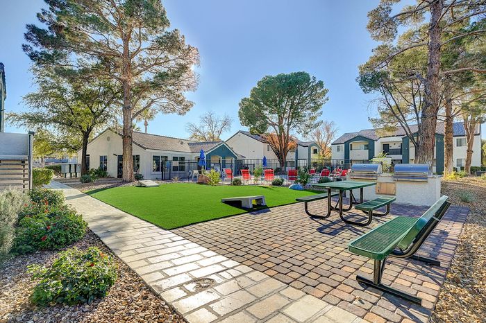 Charming outdoor community area featuring picnic benches, barbecue grills, and a lush green lawn surrounded by well-maintained landscaping and modern buildings.