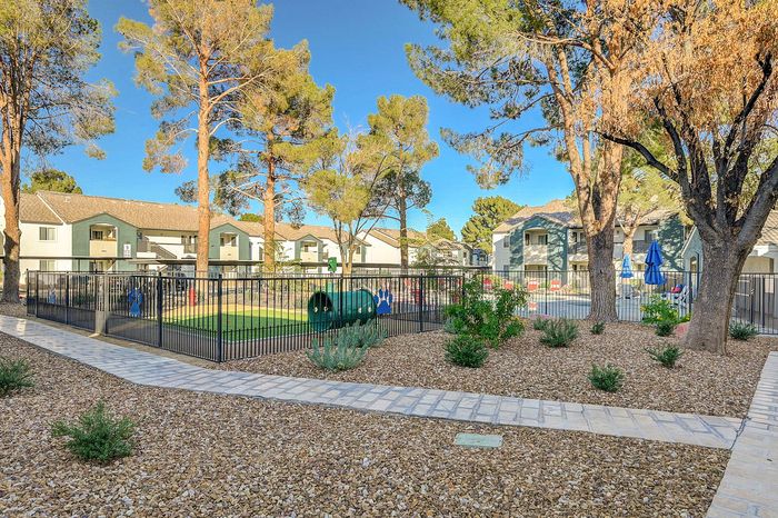 Charming apartment community with lush landscaping, vibrant playground, and inviting outdoor seating areas under clear blue skies.