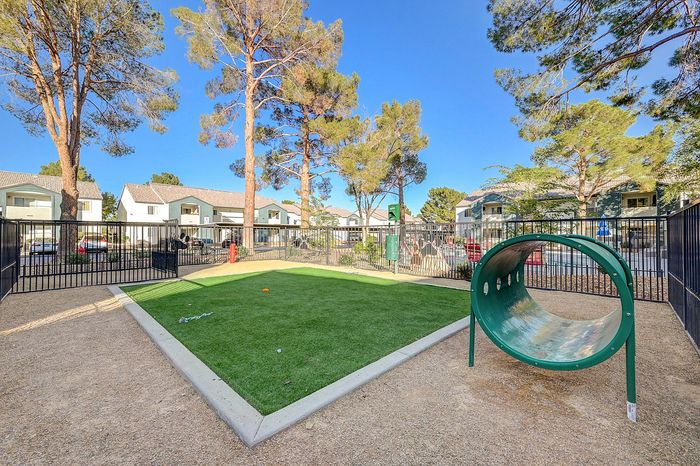 Inviting community dog park with lush green play area, surrounded by picturesque trees and charming residential homes.