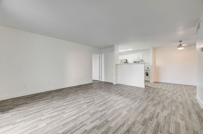 Spacious open-concept living area with modern hardwood floors, bright kitchen, and ceiling fan, perfect for entertaining.