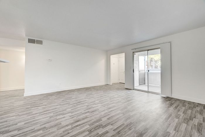 Spacious modern living room with sleek wood flooring and a bright sliding glass door leading to a balcony.
