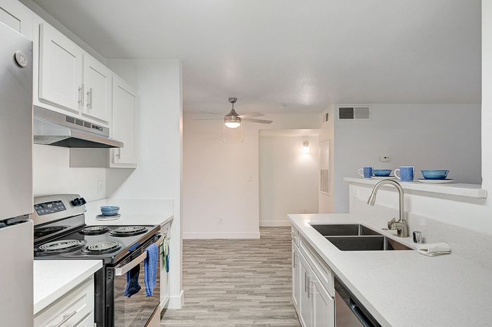 Modern kitchen with sleek white cabinetry, stainless steel appliances, and elegant countertops, leading to an open living area with a ceiling fan.
