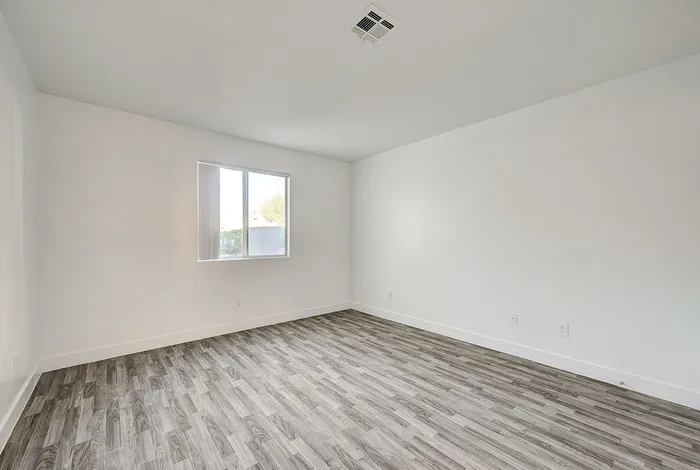 Bright and airy empty room with sleek wood flooring and a large window, perfect for customization and natural light.