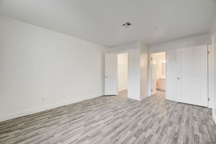 Bright and inviting unfurnished room with chic gray wood flooring, a walk-in closet, and en-suite bathroom, perfect for personal customization.
