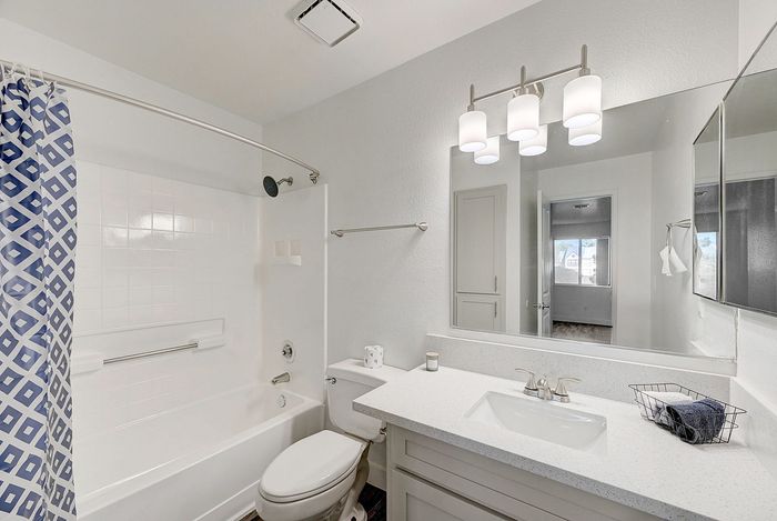 Elegant modern bathroom with sleek white fixtures, spacious vanity, and chic blue geometric shower curtain, reflecting a bright, inviting ambiance.