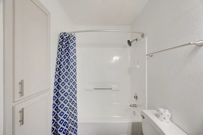 Bright modern bathroom with elegant blue-patterned shower curtain, sleek white cabinetry, and polished fixtures.
