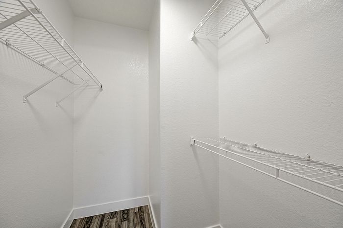 Elegant walk-in closet with ample white wire shelving and modern wood flooring, perfect for organized storage.
