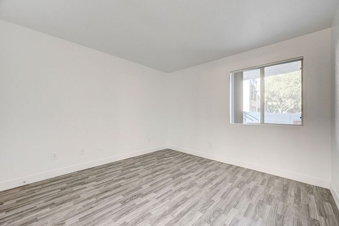 Bright and airy empty room with elegant wood flooring and a large window offering natural light.