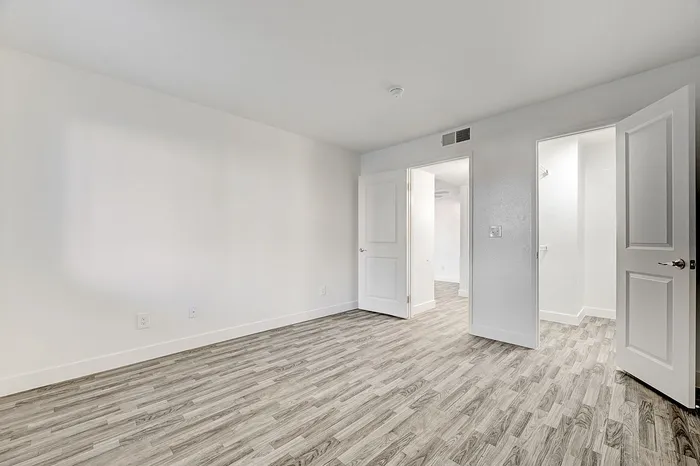 Bright and spacious room with elegant wood-style flooring, featuring double doors leading to a versatile interior space.