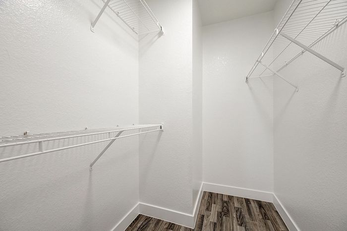 Spacious and modern walk-in closet with sleek wire shelving and elegant wood flooring, perfect for organized storage.