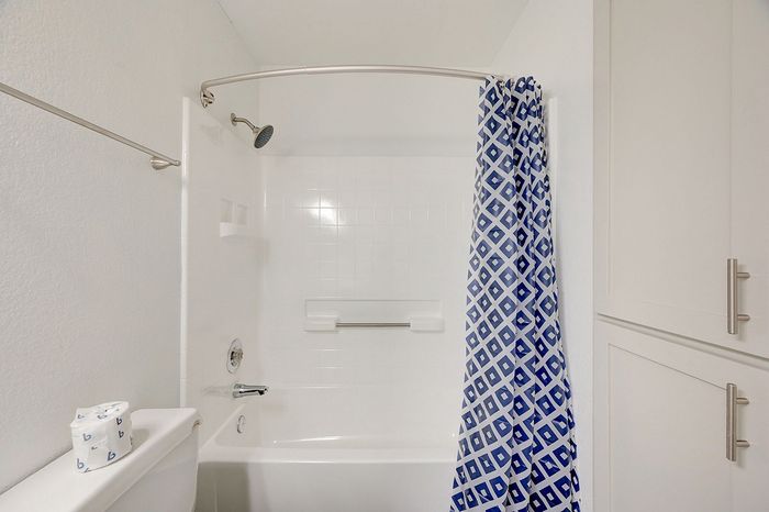 Bright, modern bathroom featuring elegant white tiles, a sleek shower setup, and a stylish blue patterned shower curtain.