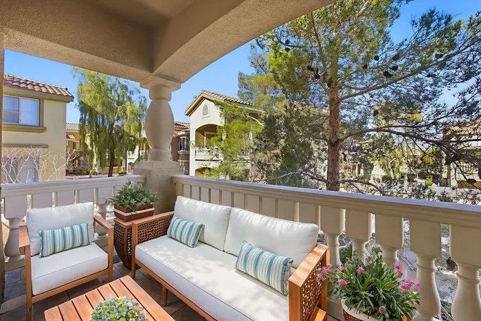 Inviting balcony adorned with plush outdoor seating and vibrant plants, offering a tranquil view of lush trees and charming townhouses.