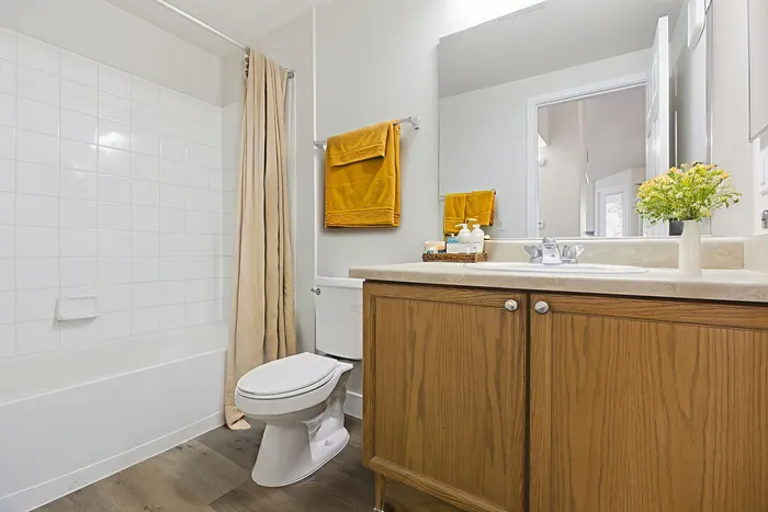 Bright and inviting bathroom featuring wooden cabinets, a sleek white countertop, and a refreshing floral arrangement for a touch of elegance.