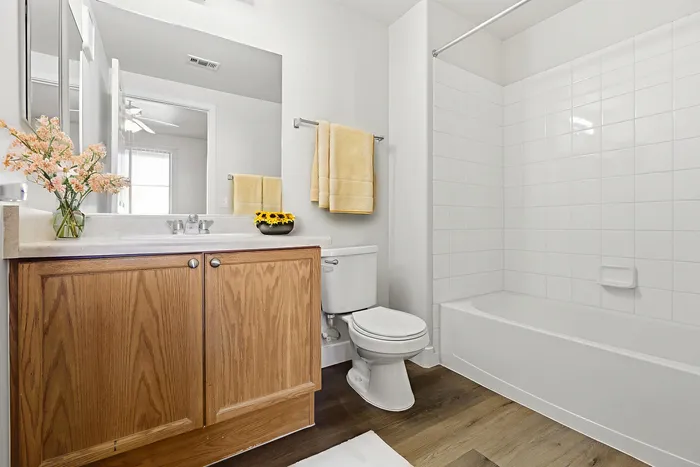 Bright and modern bathroom with elegant wooden cabinetry, fresh floral accents, and a gleaming white bathtub.
