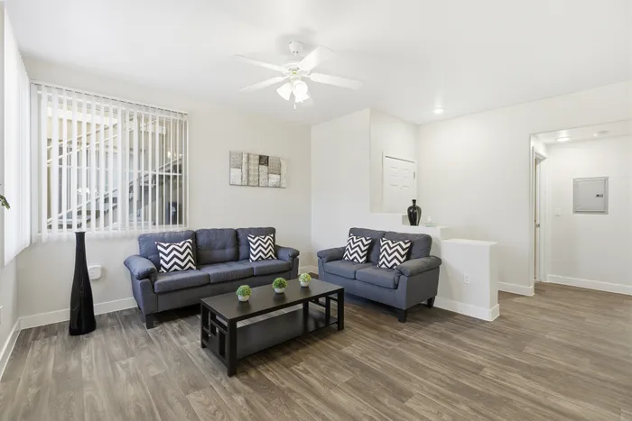 Bright and inviting living room with modern decor, featuring sleek gray sofas, decorative pillows, and stylish wood flooring, perfect for relaxation and entertaining.