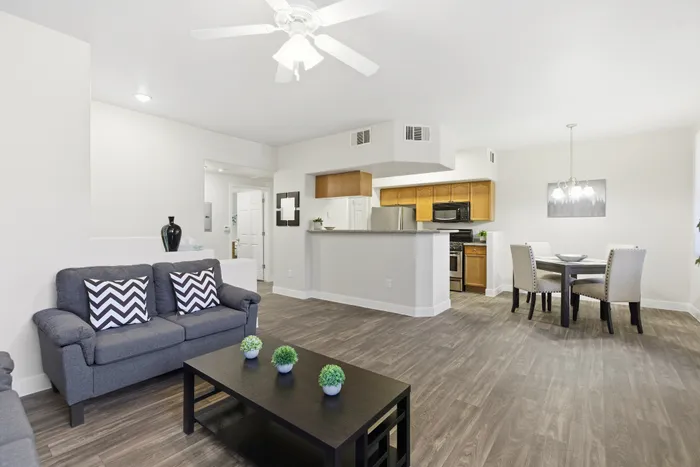 Modern open-concept living space with sleek hardwood floors, featuring a cozy grey sofa, stylish dining area, and a well-equipped kitchen with stainless steel appliances.