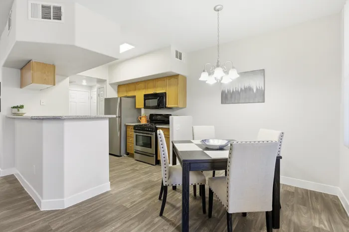Modern apartment kitchen and dining area with stainless steel appliances, elegant lighting, and stylish wooden cabinets.