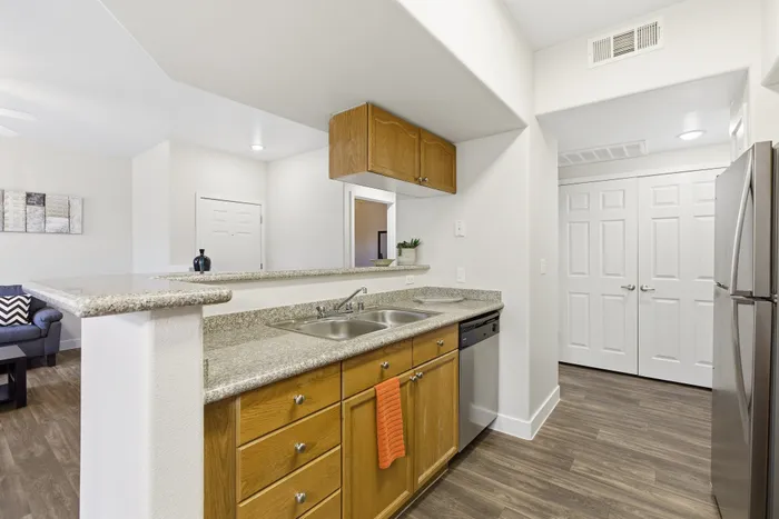 Modern kitchen with elegant granite countertops, stainless steel appliances, and chic wooden cabinetry, opening to a cozy living area with stylish decor.