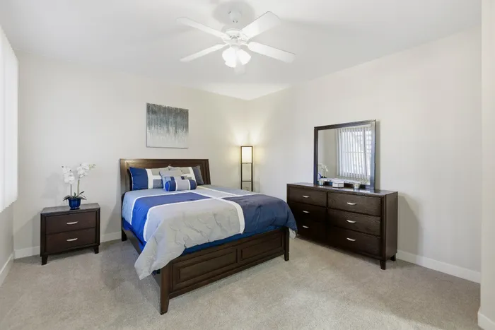 Cozy and elegantly decorated bedroom featuring a plush bed with blue accents, modern wooden furniture, and soft lighting, ideal for relaxation.