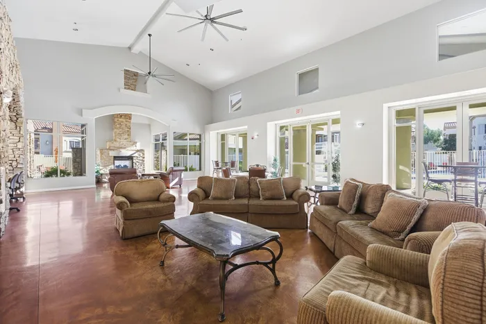 Bright and inviting open-concept living room with cozy seating, high ceilings, large windows, and an elegant stone fireplace.