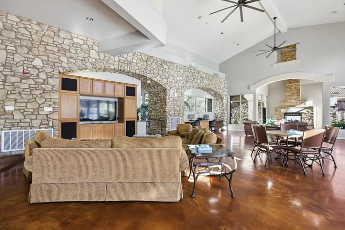 Elegant living room featuring rustic stone walls, stylish beige couches, and a modern TV setup, complemented by large windows and ceiling fans.