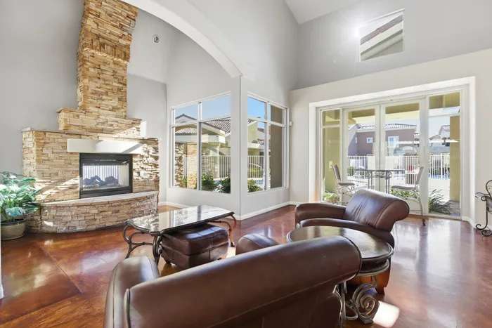 Sunlit living room boasting elegant leather seating and a striking stone fireplace, complemented by expansive windows with a scenic outdoor view.