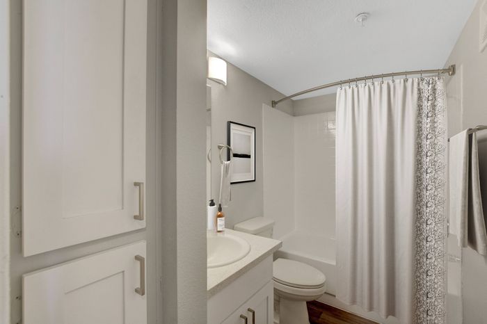 Bright and modern bathroom featuring sleek cabinetry, an elegant countertop, and a classic shower with white curtains.