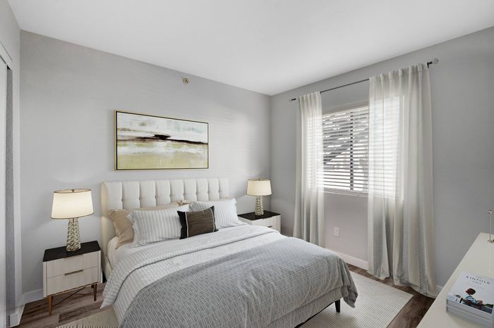 Inviting bedroom with modern decor, featuring a plush white bed, elegant side tables, abstract wall art, and a sunlit window with soft drapery.