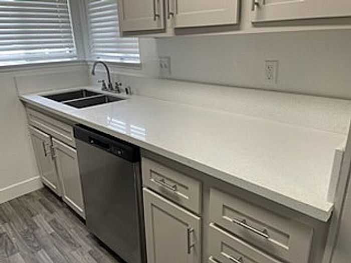 Modern kitchen with sleek white countertops, stainless steel dishwasher, and ample storage in an inviting apartment setting.