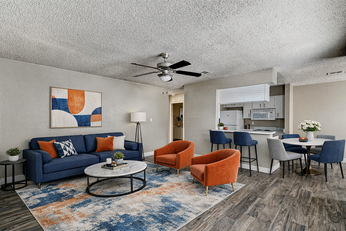 Modern open concept living space with vibrant decor and cozy furnishings, featuring a stylish blue sofa, orange accent chairs, and a sleek kitchen bar.
