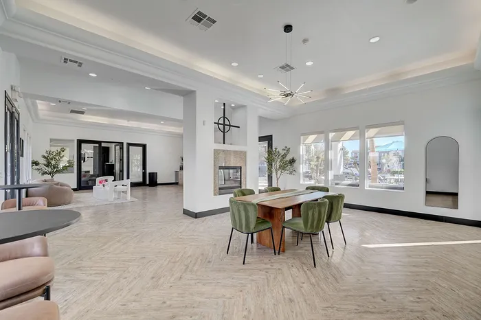 Spacious and modern living area with sleek wood flooring, stylish green chairs around a wooden table, and abundant natural light streaming through large windows.