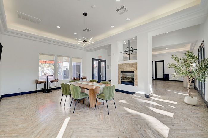 Modern communal area filled with natural light, featuring elegant green chairs, a stylish wooden table, and a contemporary fireplace. Ideal for gatherings and relaxation.