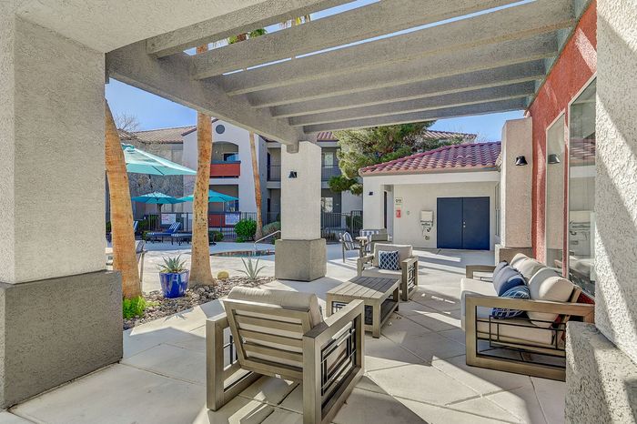 Chic apartment patio with modern outdoor seating, vibrant blue accents, and a view of the inviting pool area surrounded by palm trees.