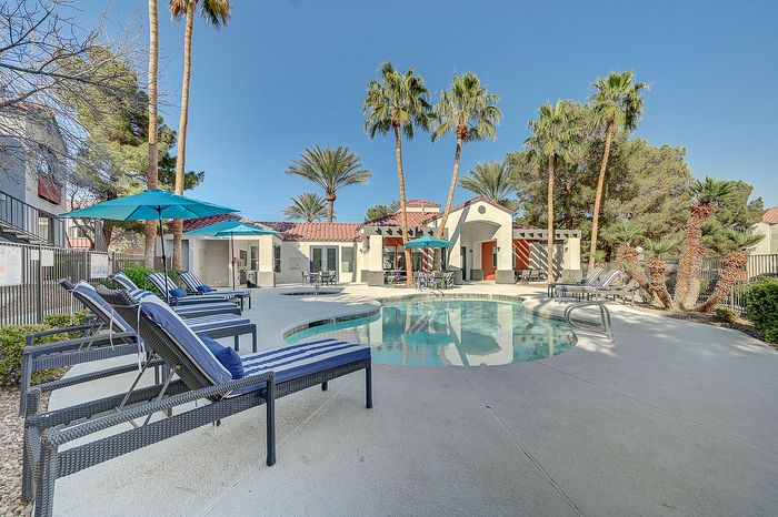 Inviting outdoor pool area with stylish lounge chairs, vibrant umbrellas, and lush palm trees, offering a perfect relaxation spot.