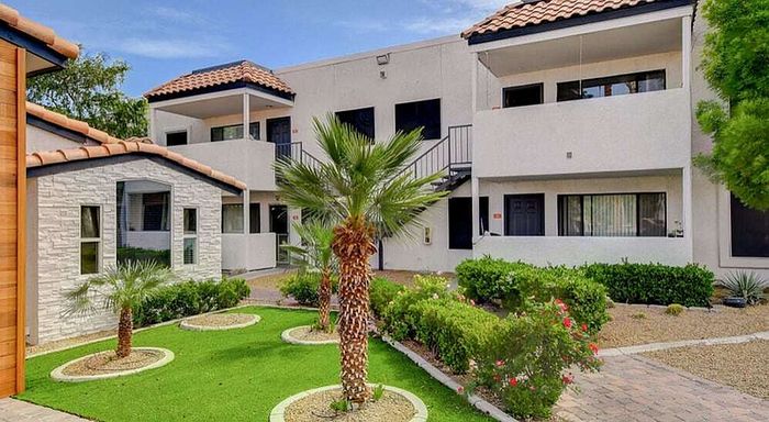 Charming Mediterranean-style apartment complex with lush landscaping, vibrant green lawns, and elegant terraces.