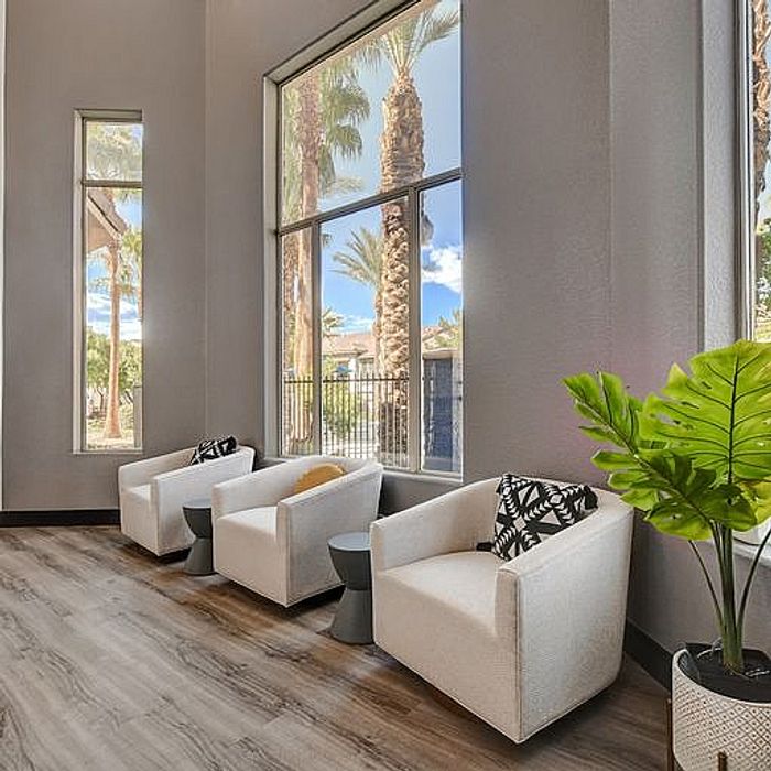 Elegant apartment lounge featuring modern armchairs, high ceilings, and large windows with views of palm trees and a sunny sky.