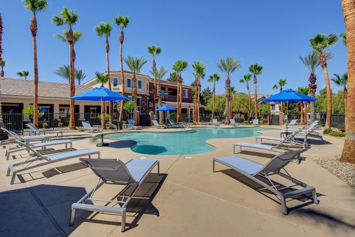 Luxurious poolside oasis with palm trees, modern lounge chairs, and vibrant blue umbrellas under a clear blue sky.