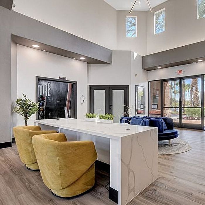 Chic modern living space with high ceilings, stylish yellow chairs, and an elegant marble counter near a bright entrance with large windows.
