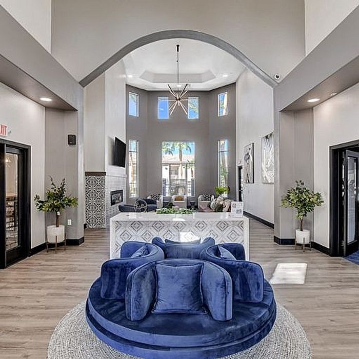 Elegant apartment lobby with high ceilings, modern chandelier, cozy blue seating, and stylish decor.