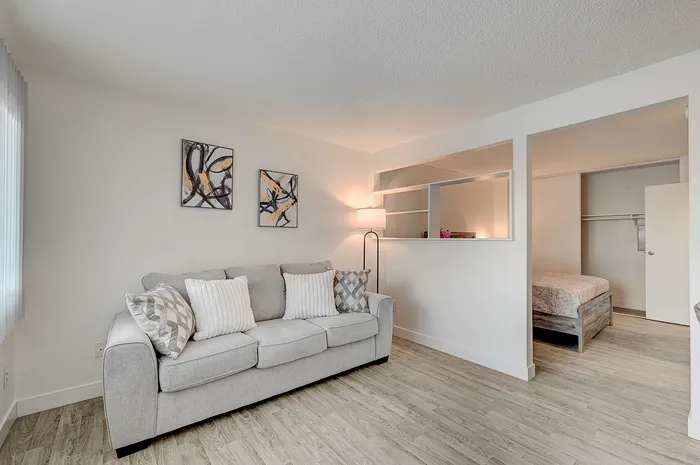 Inviting living room featuring a chic gray sofa with plush pillows, modern abstract art, and adjacent cozy bedroom with elegant shelving.