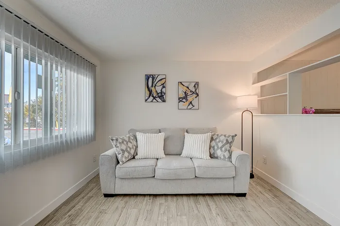 Elegant living room with a cozy beige sofa, stylish artwork, and abundant natural light through large windows.