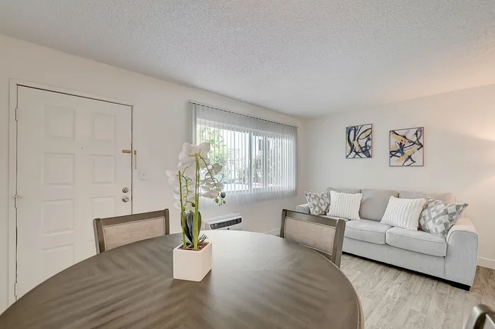 Bright and inviting living space featuring a cozy sofa, modern art, and a stylish dining area with natural light streaming through large windows.